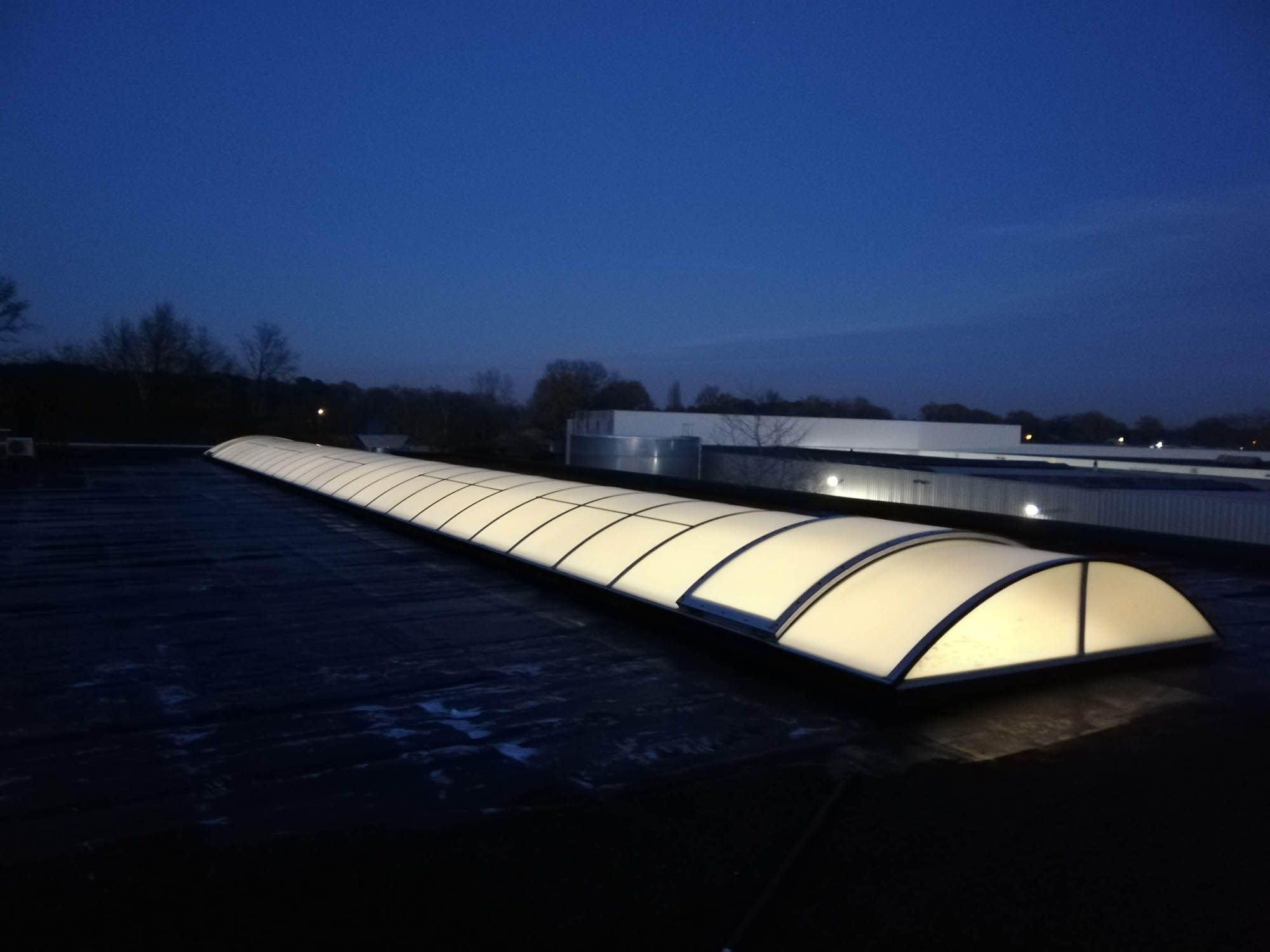 Verlichte gebogen lichtstraat op een plat dak bij avond, na reiniging
