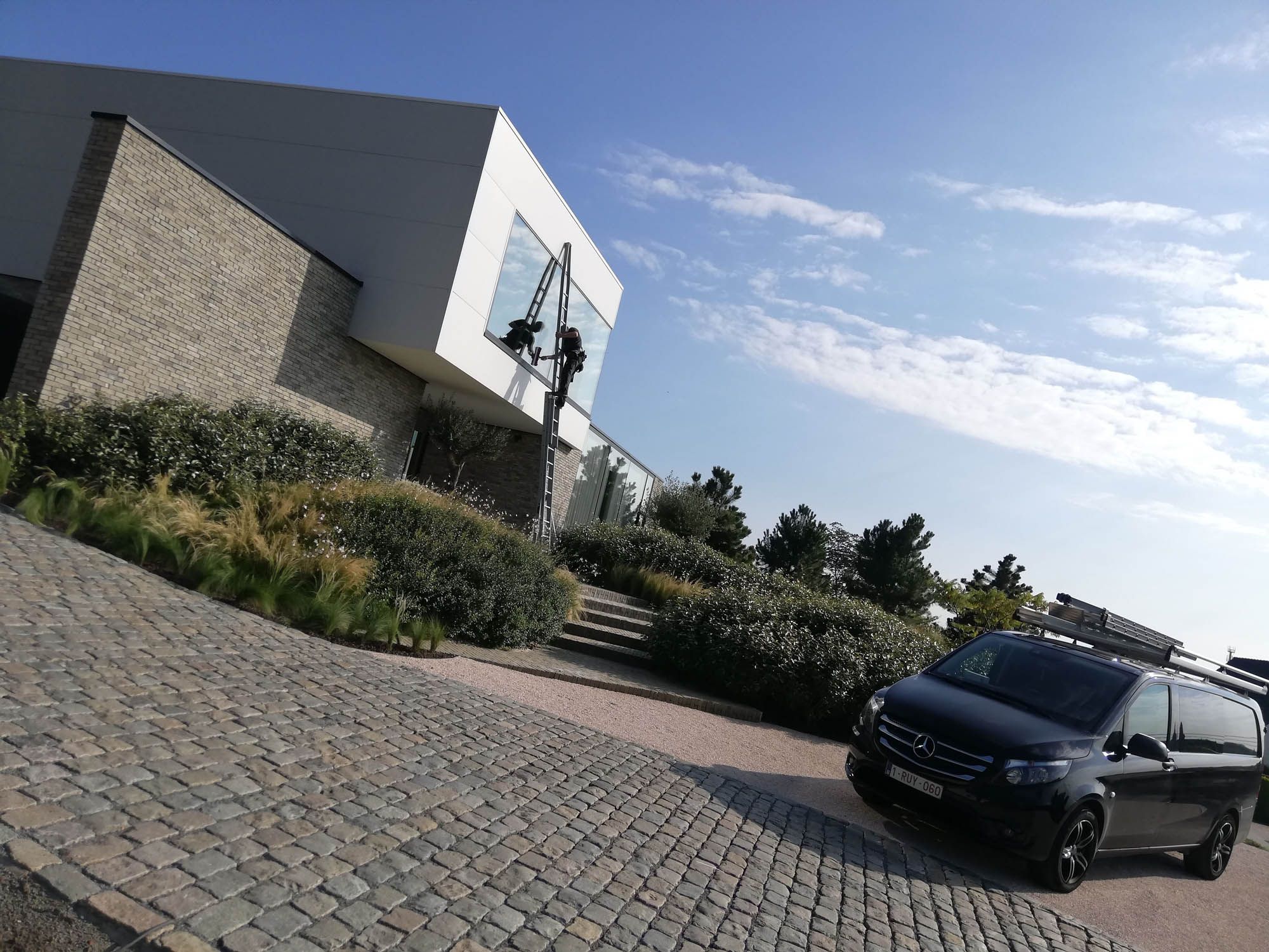 Modern kantoorgebouw in natuursteen met bestelwagen en ladders van Glaswas Verelst