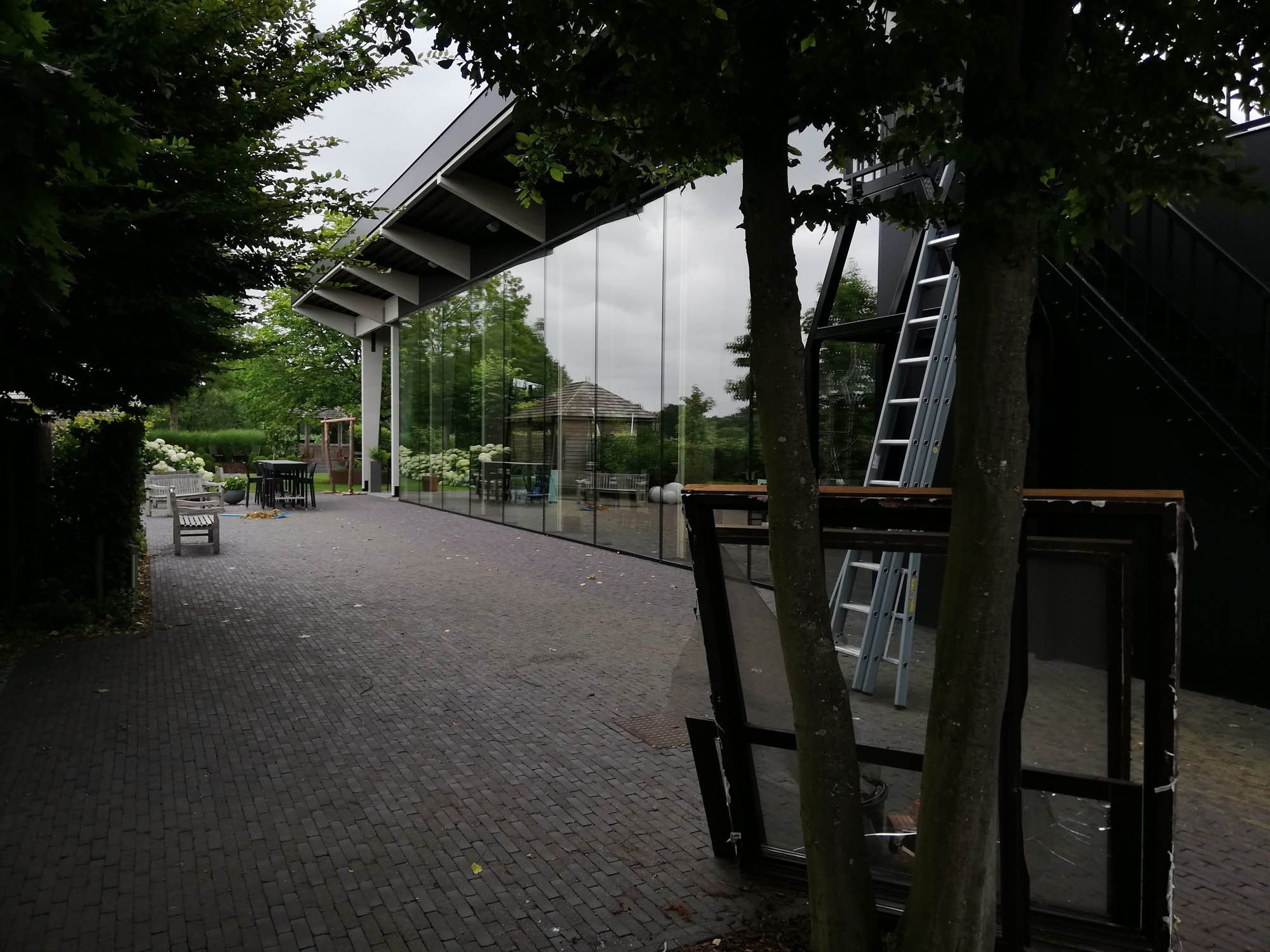 Lange glasgevel langs een overdekte doorgang met ladder tijdens de glasbewassing