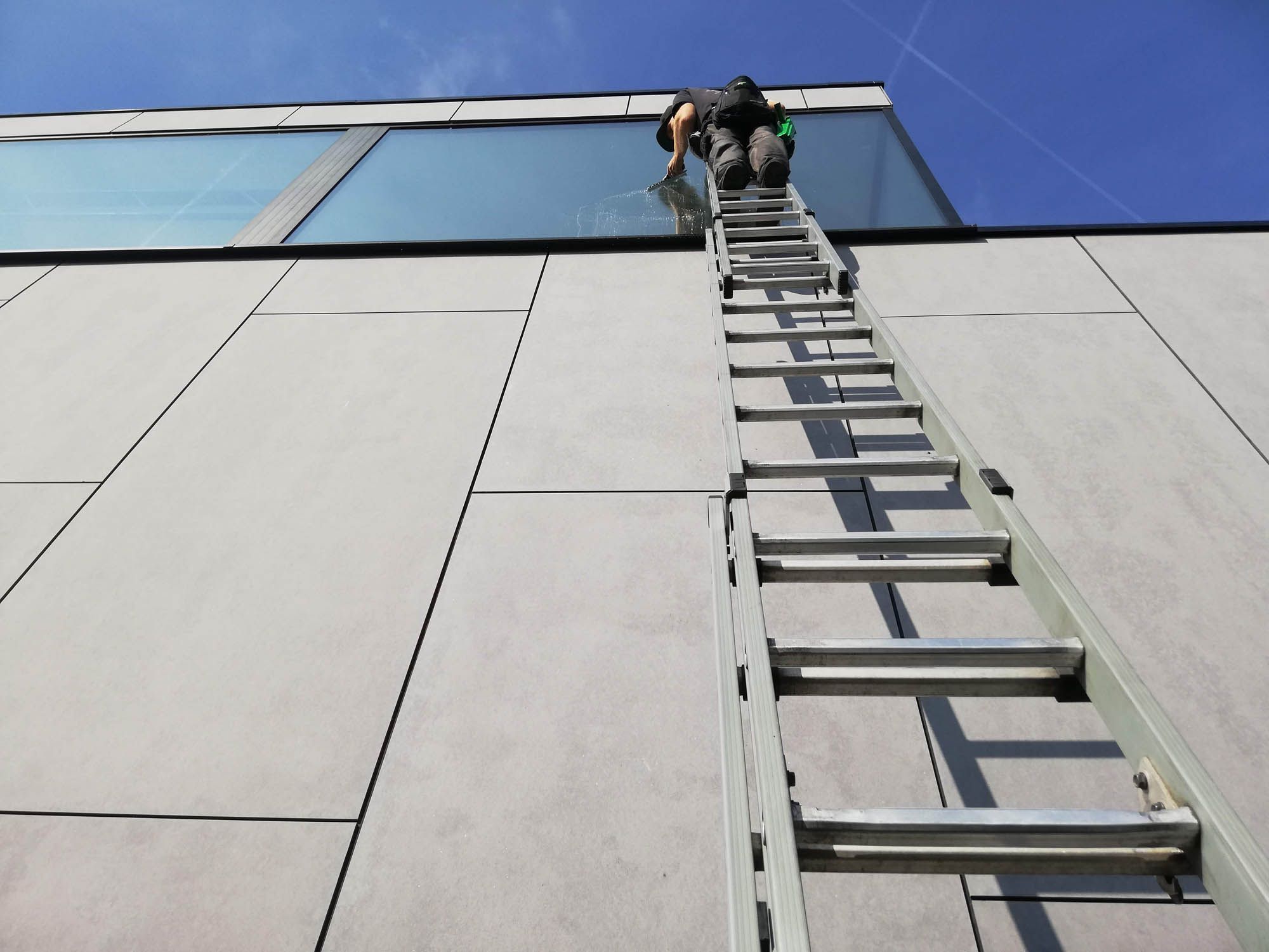 Ramenwasser op ladder reinigt de bovenste glasgevel van een bedrijfspand