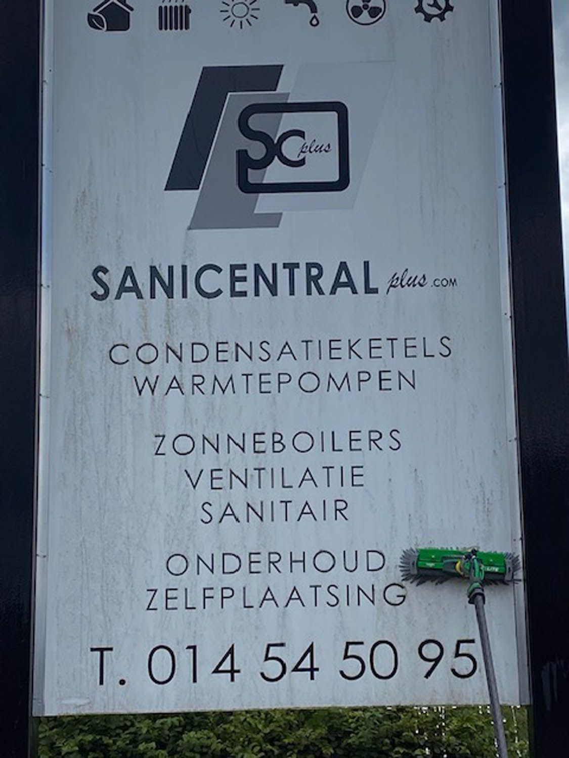 Reclamebord van Sanicentral wordt gereinigd met een wasborstel op telescoopsteel